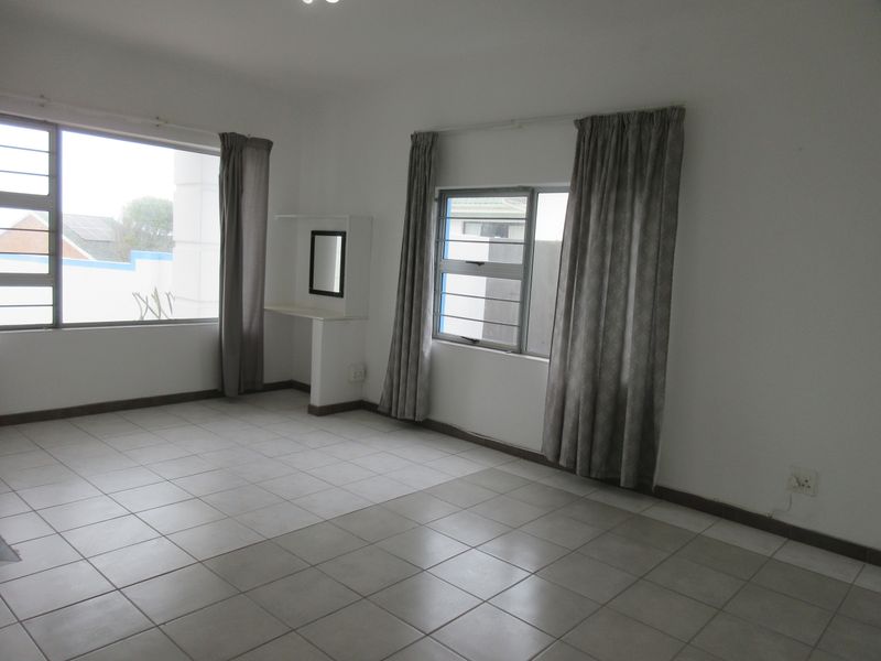 A spacious, empty bedroom featuring neutral tiled flooring, large windows with security bars, and a built-in vanity shelf.