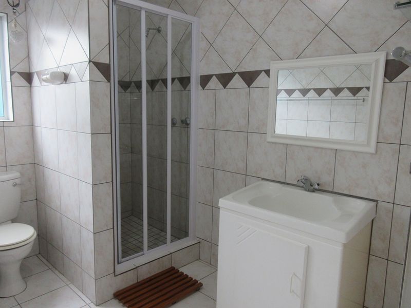 A functional bathroom featuring a shower enclosure, vanity cabinet with basin, and toilet, finished with neutral ceramic wall and floor tiling.