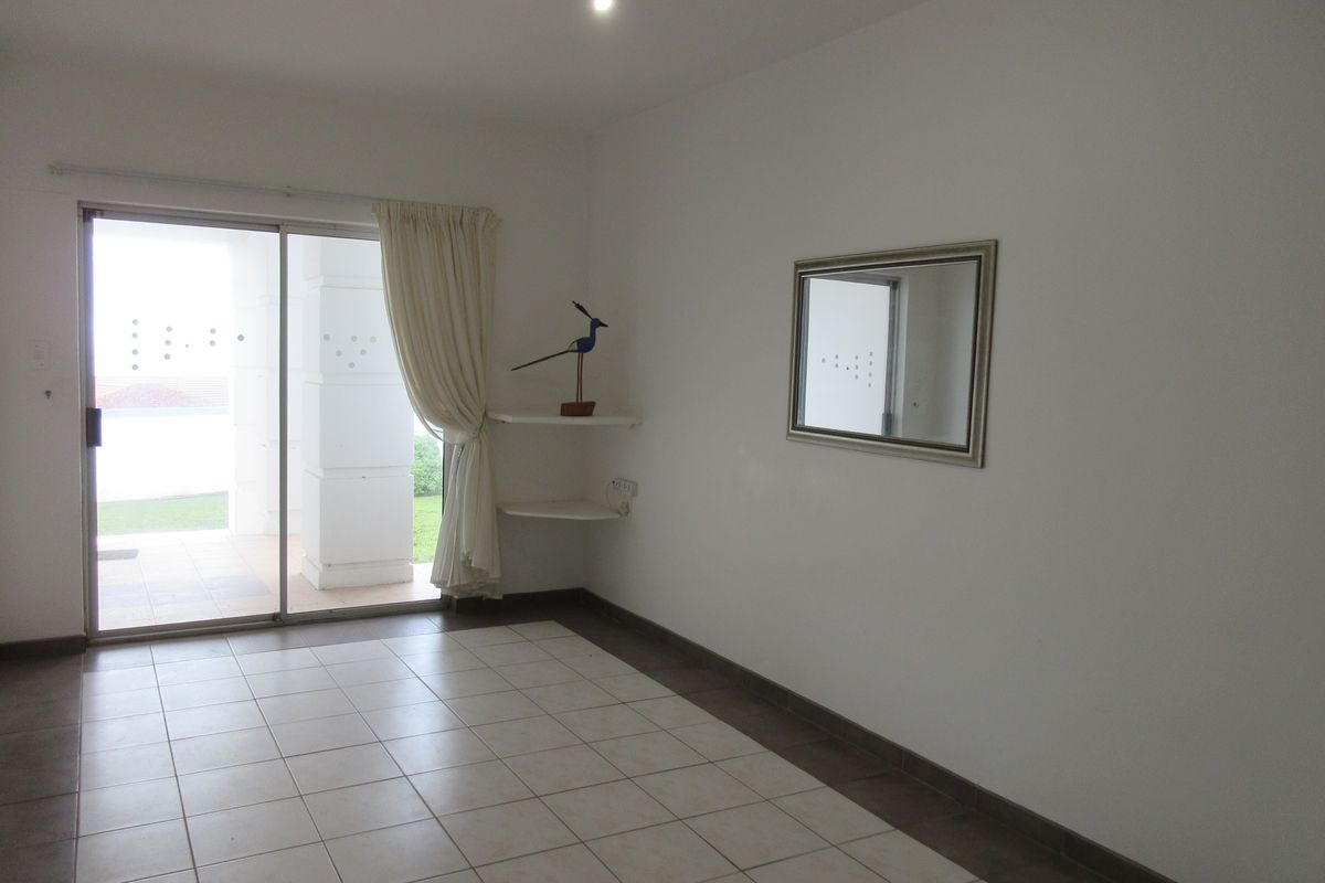 An empty living room featuring ceramic floor tiles, built-in corner shelving, and a sliding glass door providing access to an outdoor patio area.