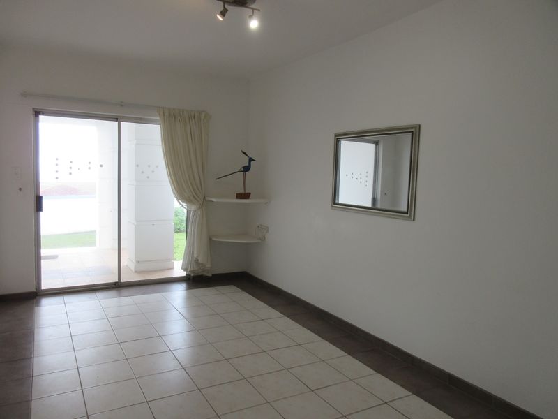 An empty living room featuring ceramic floor tiles, built-in corner shelving, and a sliding glass door providing access to an outdoor patio area.