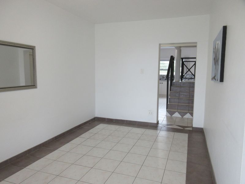 An empty living area featuring neutral tiled flooring, leading to a staircase and an adjacent room.