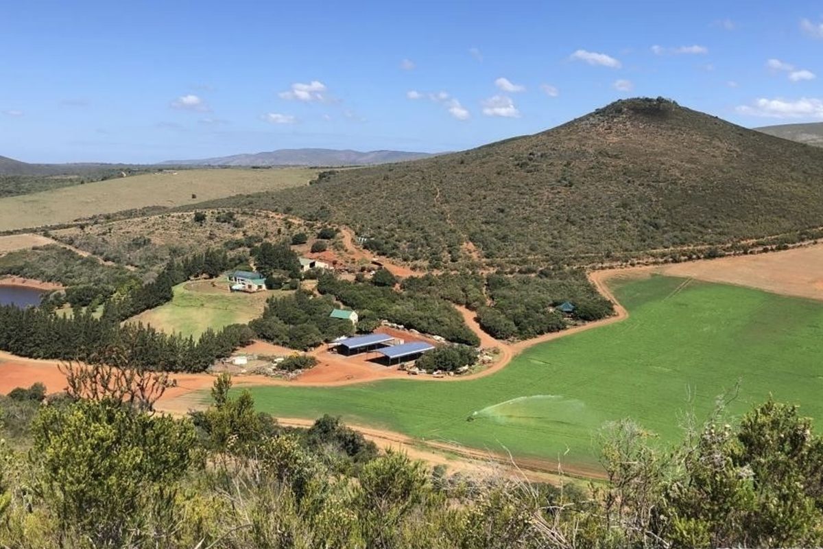 An elevated aerial view of a rural farm property featuring agricultural fields, a dam, and various farm infrastructure buildings set against a hilly landscape.