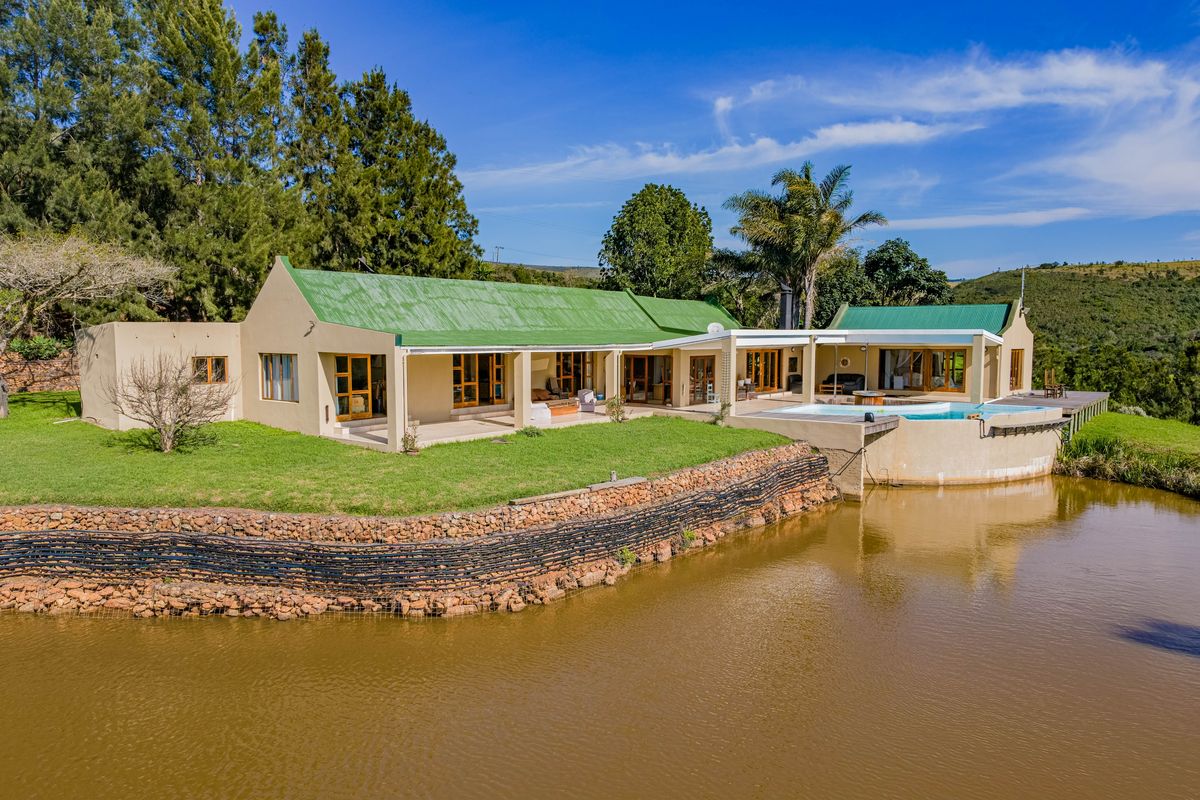 Rear view of a farm property featuring a swimming pool, covered patio, and timber decking overlooking a private pond and landscaped grounds.