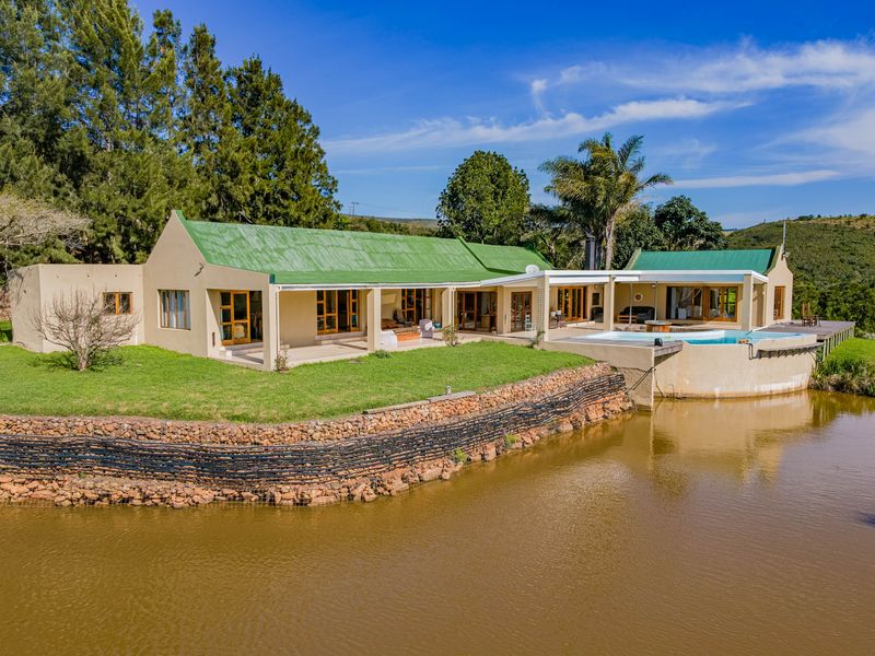 Rear view of a farm property featuring a swimming pool, covered patio, and timber decking overlooking a private pond and landscaped grounds.