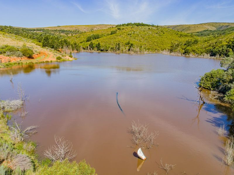 An aerial view of a large farm dam surrounded by rolling hills and natural vegetation.