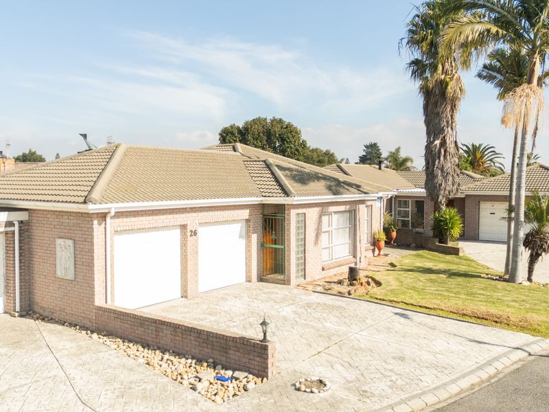 Front elevation of a brick-faced house featuring a double garage, paved driveway, and established garden with palm trees.