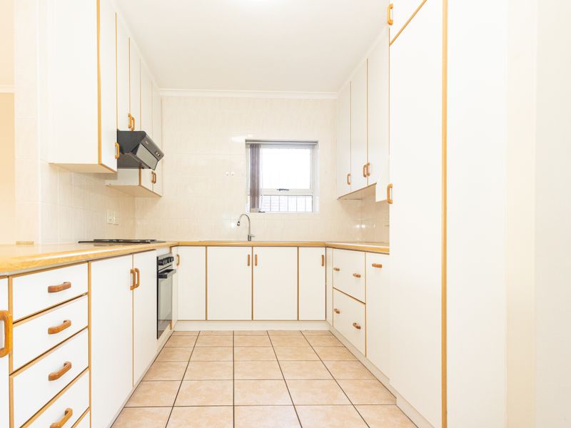 A functional, galley-style kitchen featuring white cabinetry with wood trim, tiled flooring, and integrated appliances, offering a clean and neutral space.