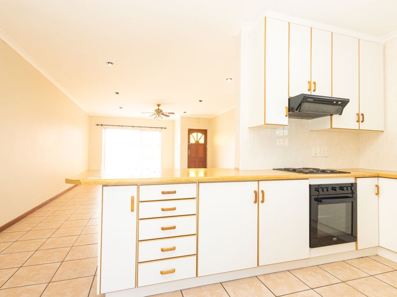 Open-plan kitchen and living area featuring white cabinetry, built-in oven, gas hob, and neutral tiled flooring throughout the space.