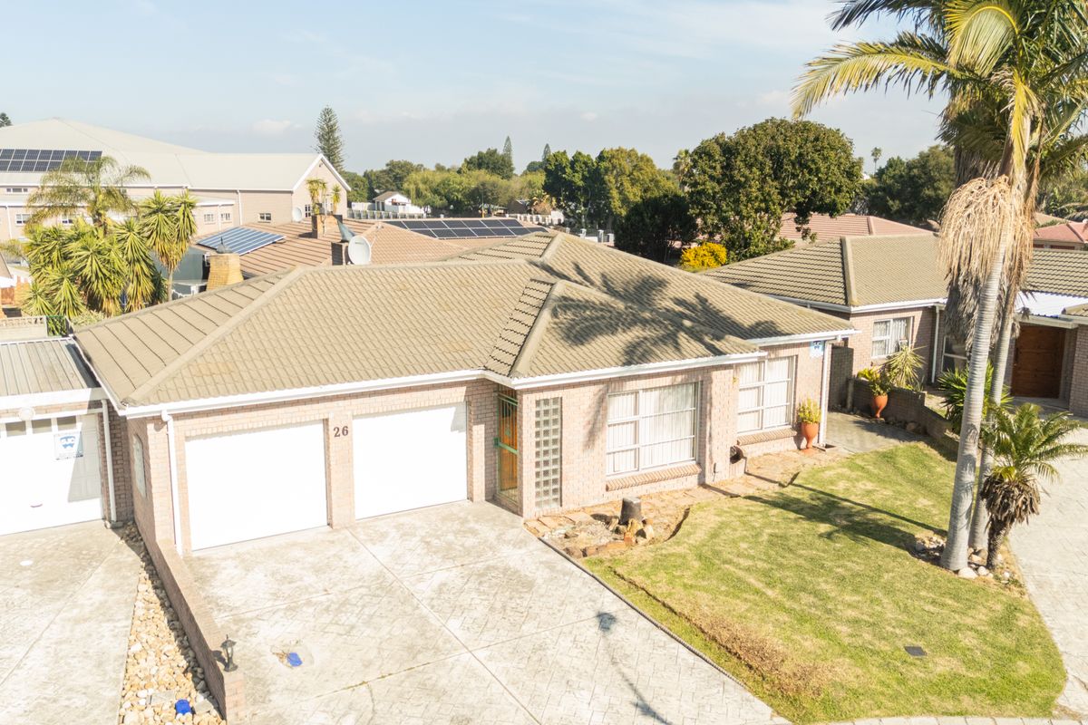 Aerial view of a single-story brick house featuring a tiled roof, double garage, paved driveway, and a well-maintained front lawn.