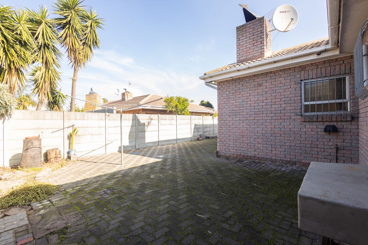A rear exterior view featuring a paved patio area, brick chimney, and precast concrete boundary wall.