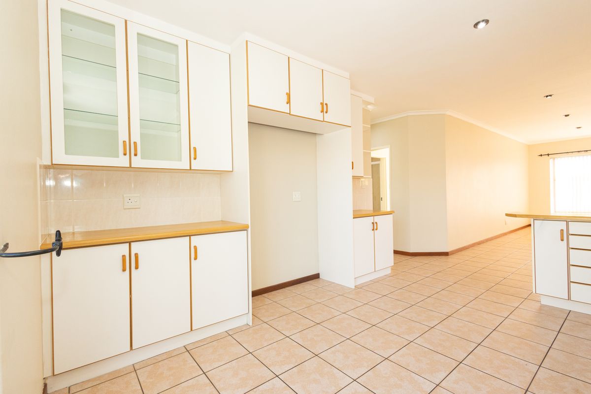 A bright, open-plan kitchen featuring white cabinetry with timber-look trim, tiled flooring, and ample storage space, presenting a clean and functional layout.