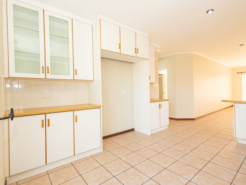 A bright, open-plan kitchen featuring white cabinetry with timber-look trim, tiled flooring, and ample storage space, presenting a clean and functional layout.