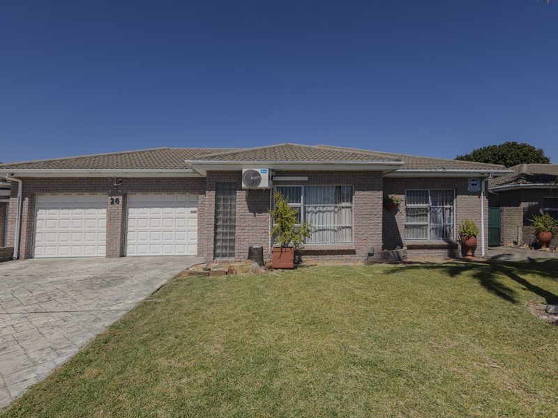 Front elevation of a single-story brick house featuring a double garage, paved driveway, and well-maintained front lawn under a clear blue sky.