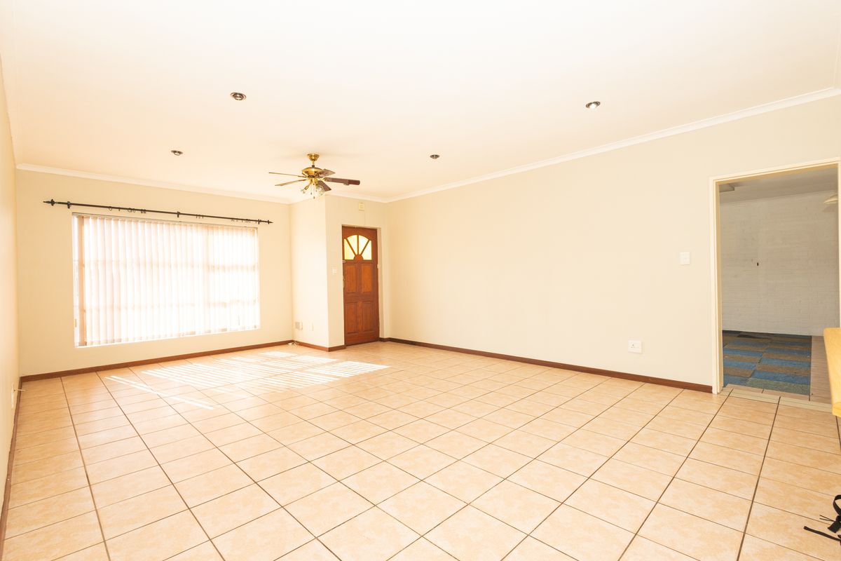 Spacious, light-filled living area featuring neutral tiled flooring, recessed lighting, a ceiling fan, and direct access to an adjoining room.