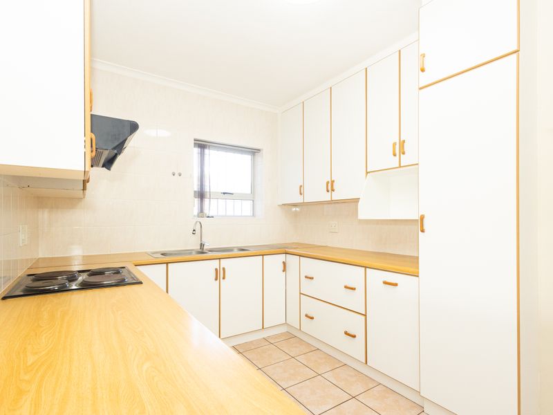 A clean, functional kitchen featuring white cabinetry, wood-look laminate countertops, an electric hob, and tiled splashbacks, offering a bright and practical workspace.