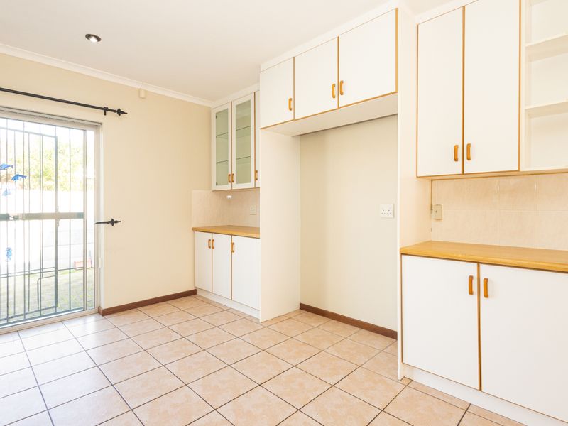 A clean, functional scullery area featuring ample built-in cabinetry, laminate countertops, tiled flooring, and direct access to the exterior via a security gate.