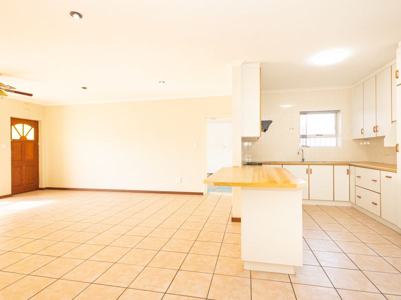 Spacious open-plan living and kitchen area featuring tiled flooring, built-in cabinetry, a wooden breakfast bar, and a ceiling fan.