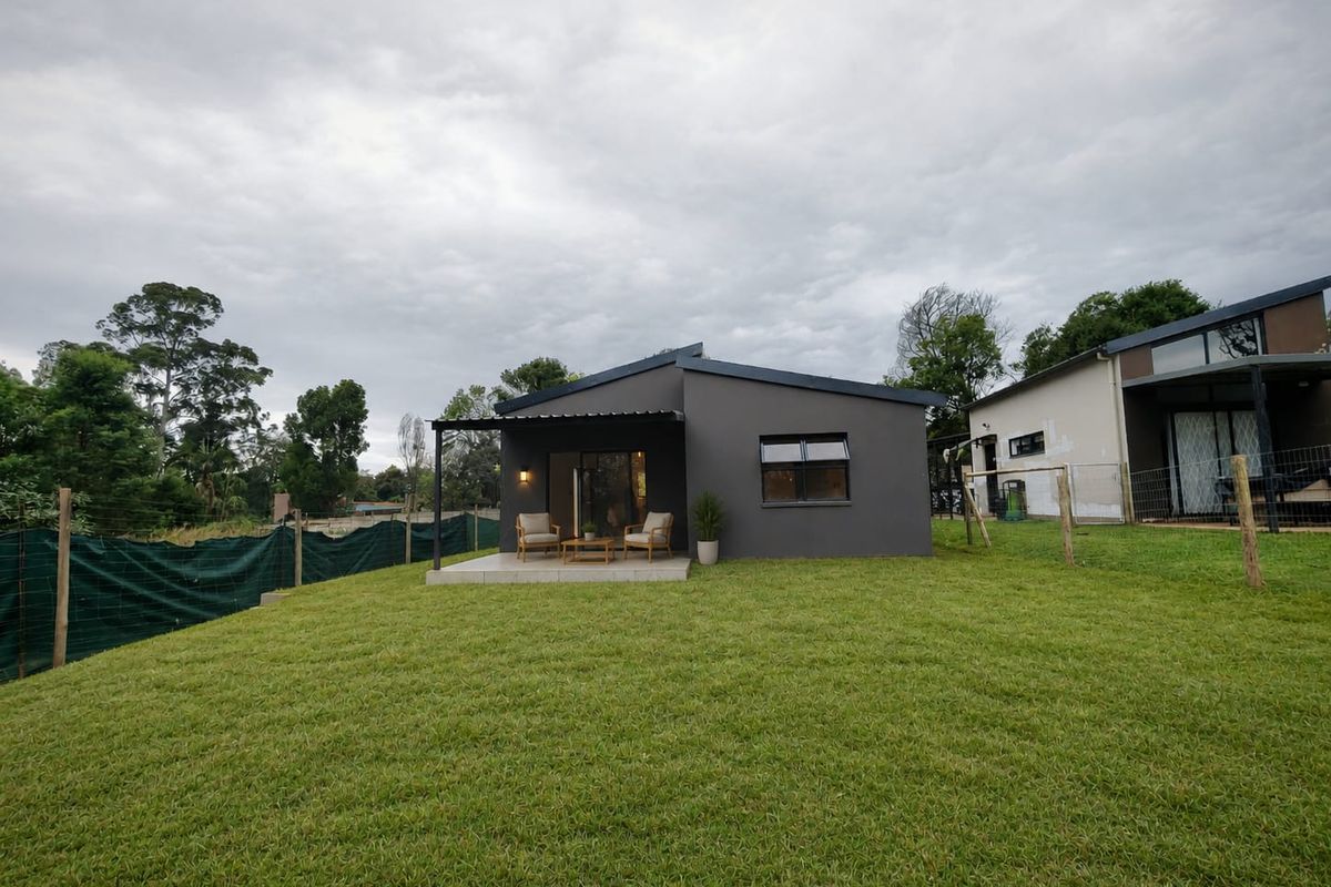 Rear view of the townhouse featuring a covered patio, a well-maintained lawn, and modern dark grey exterior finishes.