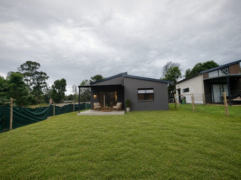 Rear view of the townhouse featuring a covered patio, a well-maintained lawn, and modern dark grey exterior finishes.