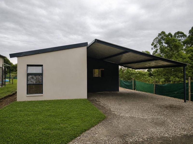 Modern townhouse exterior featuring a spacious gravel carport, clean rendered facade, and well-maintained lawn area.