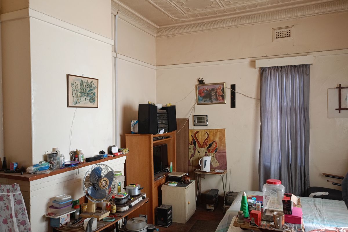 A living room featuring an original ornate pressed metal ceiling and a fireplace mantle, currently requiring cosmetic updates and repairs to walls.