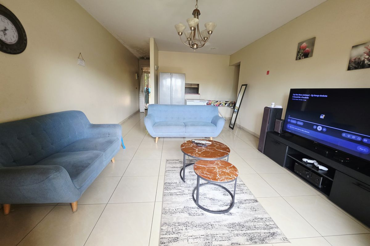 Spacious living room featuring neutral tiled flooring and a central ceiling light fixture, with visible signs of ceiling water damage.