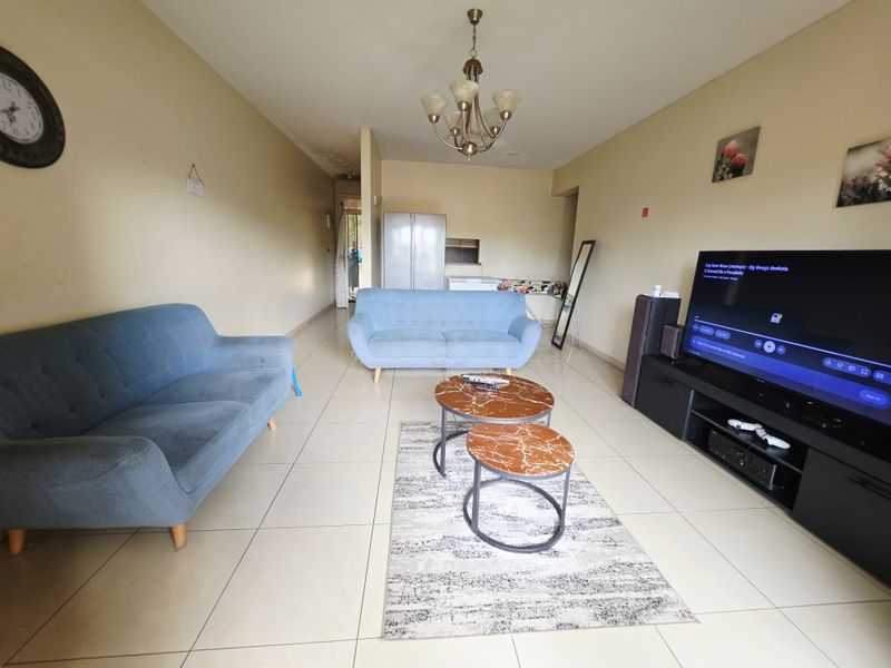 Spacious living room featuring neutral tiled flooring and a central ceiling light fixture, with visible signs of ceiling water damage.