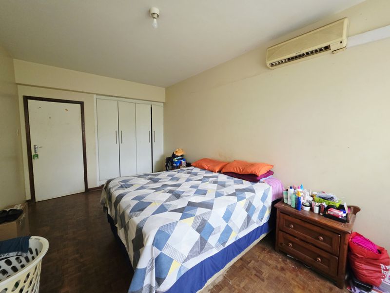 A bedroom featuring parquet flooring, built-in cupboards, and a wall-mounted air conditioning unit, offering a functional space ready for cosmetic updates.