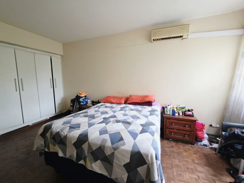 A bedroom featuring parquet flooring, a built-in wardrobe, and a wall-mounted air conditioning unit.