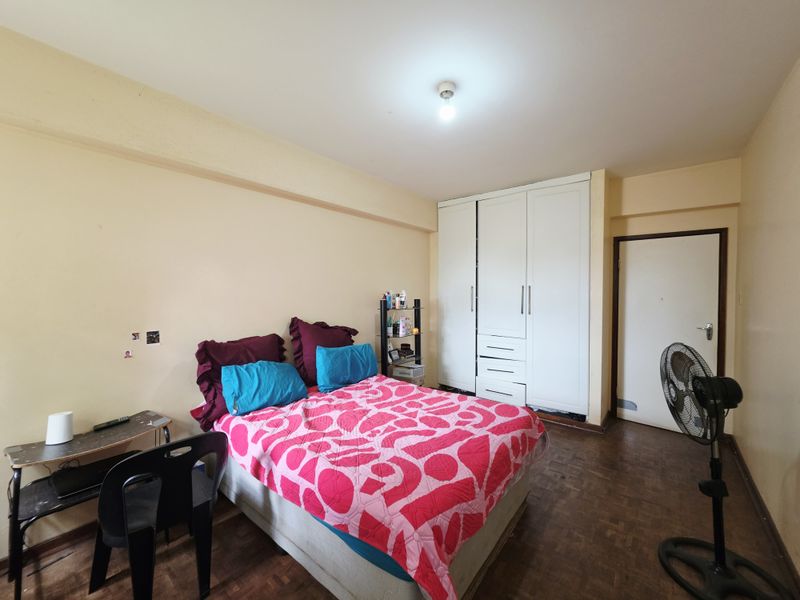 A bedroom featuring parquet flooring and a built-in white wardrobe, requiring cosmetic updates to the wall finishes and general maintenance.