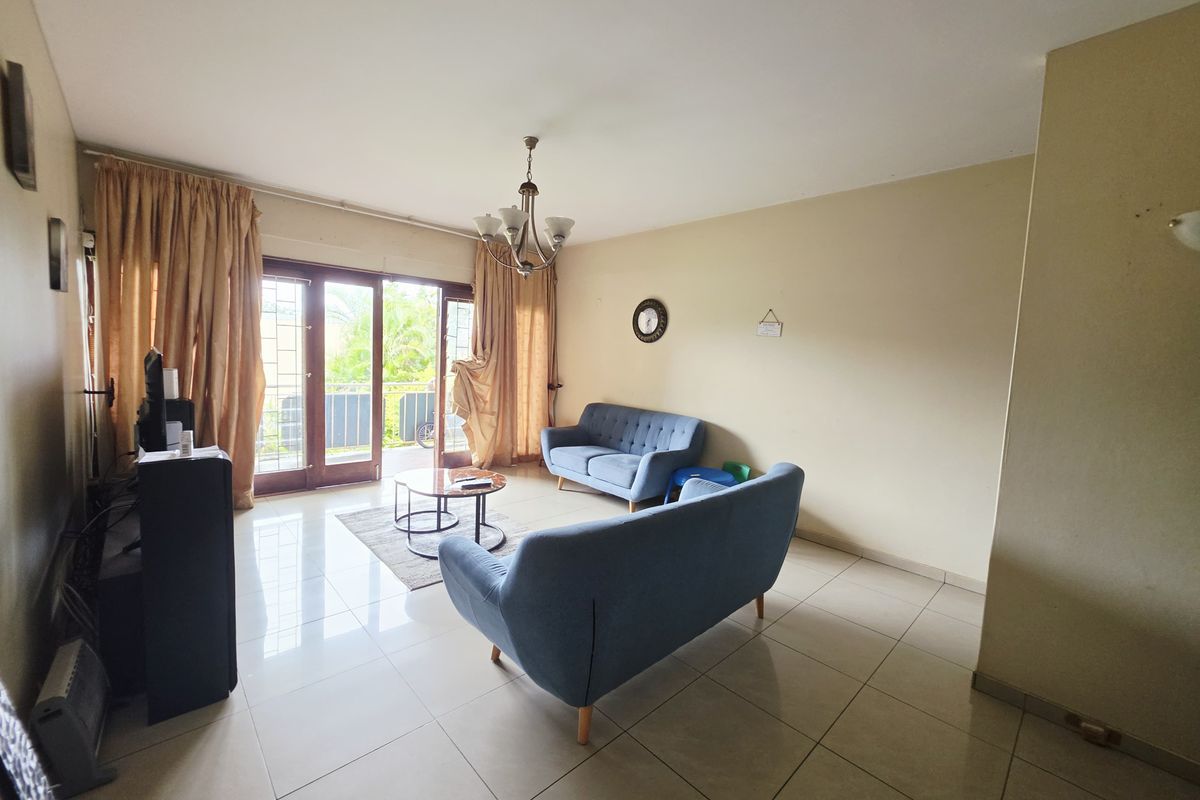 A spacious living room featuring tiled flooring and a large sliding glass door that provides access to an outdoor balcony area.