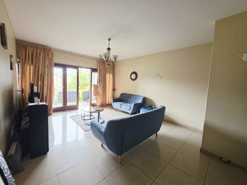 A spacious living room featuring tiled flooring and a large sliding glass door that provides access to an outdoor balcony area.