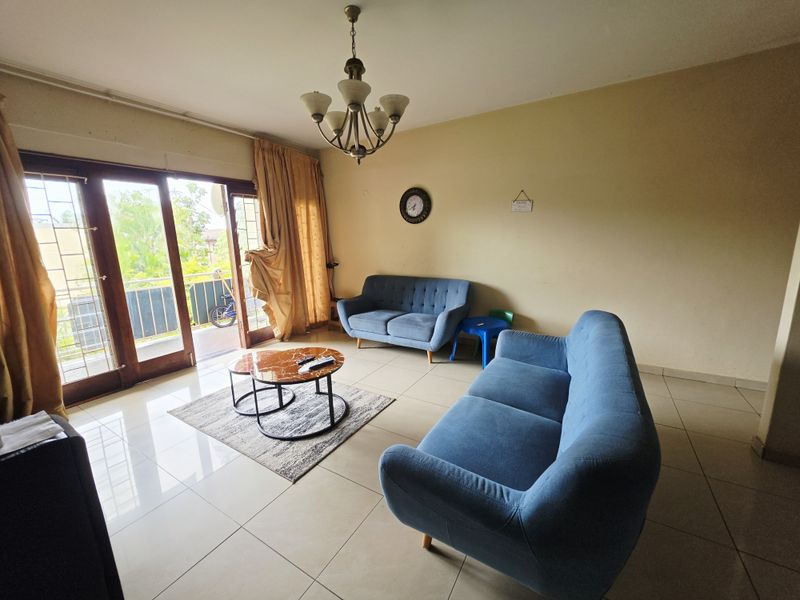 A living room featuring tiled flooring, a central chandelier, and large sliding glass doors that provide access to an outdoor balcony area.