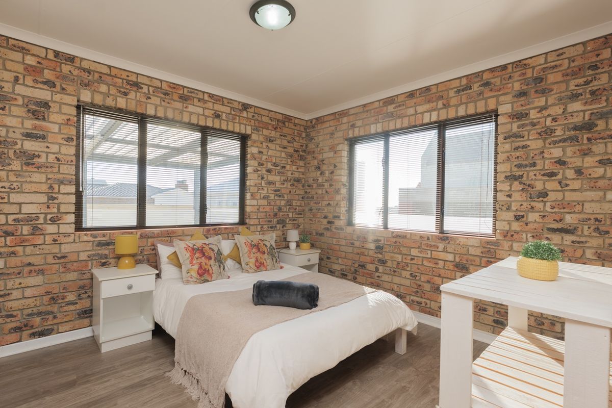 A well-lit bedroom featuring exposed brick walls, laminate flooring, and built-in storage, offering a warm and textured aesthetic.
