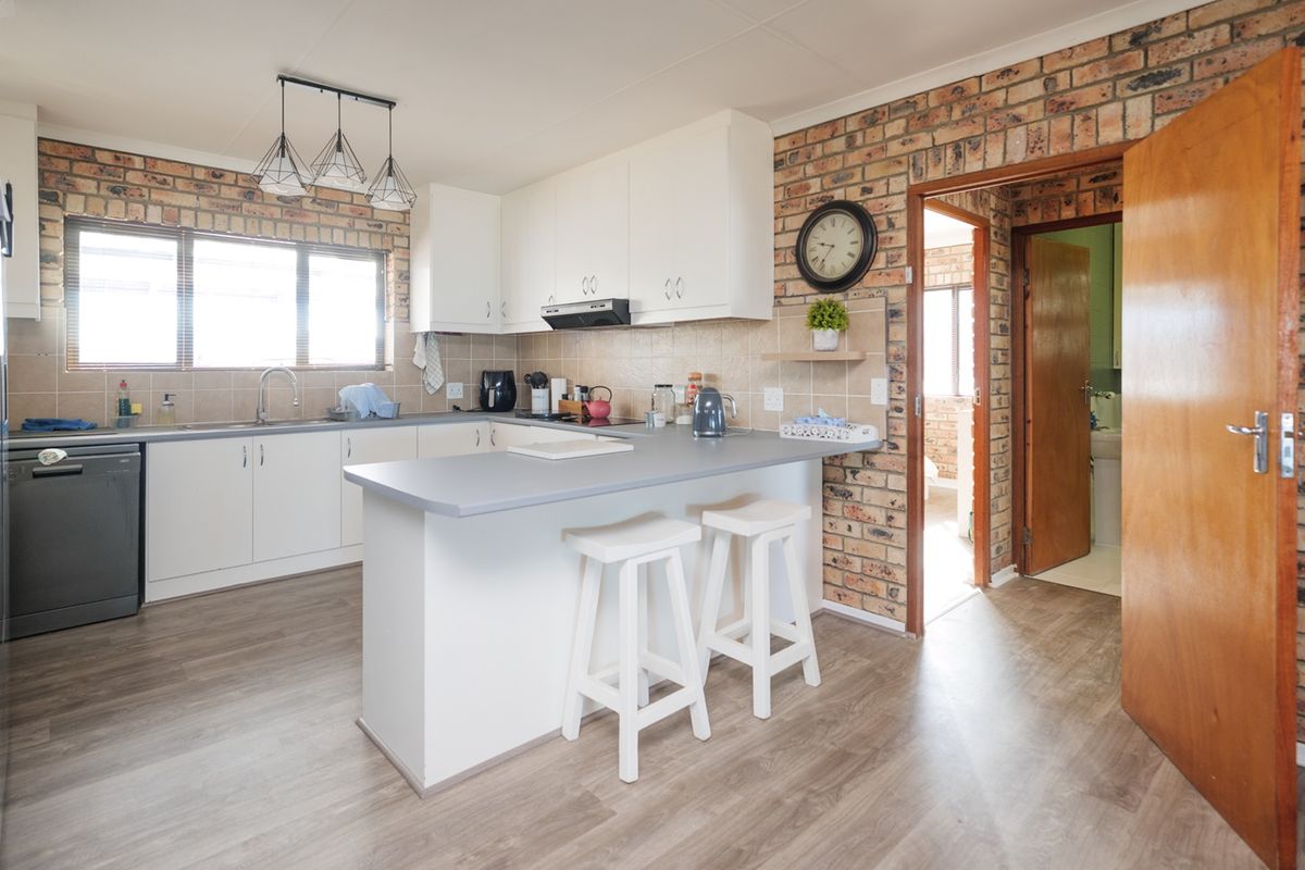 A functional kitchen featuring white cabinetry, laminate countertops, a breakfast bar, and distinctive exposed brick walls, providing a warm and practical cooking space.