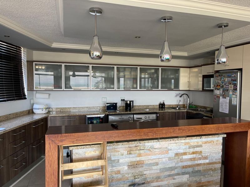 Modern kitchen featuring granite countertops, stone-clad breakfast bar, ample cabinetry, and stylish pendant lighting, creating a functional and contemporary cooking space.