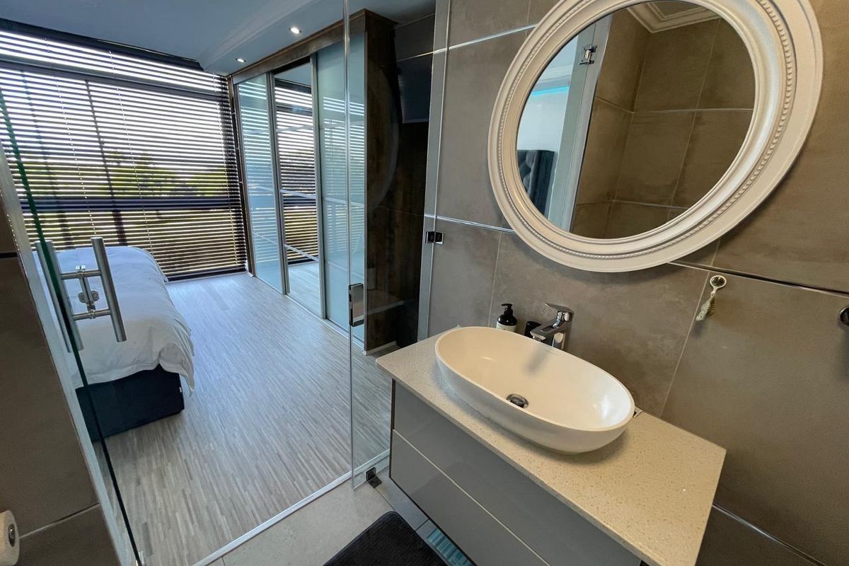 Modern bathroom featuring a sleek vanity with countertop basin, glass shower enclosure, and integrated sliding door wardrobe in a contemporary open-plan bedroom layout.