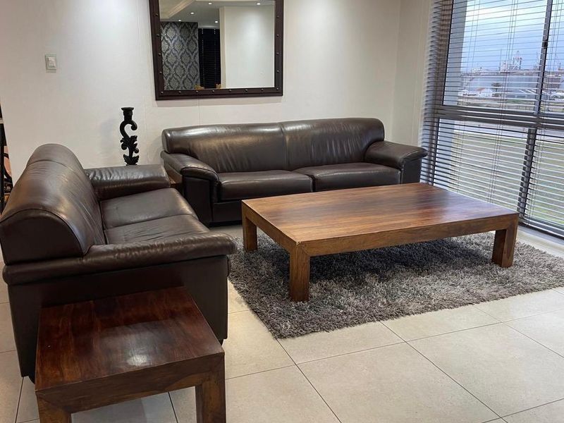 A bright living room featuring large windows with venetian blinds, neutral tiled flooring, and recessed ceiling lighting.
