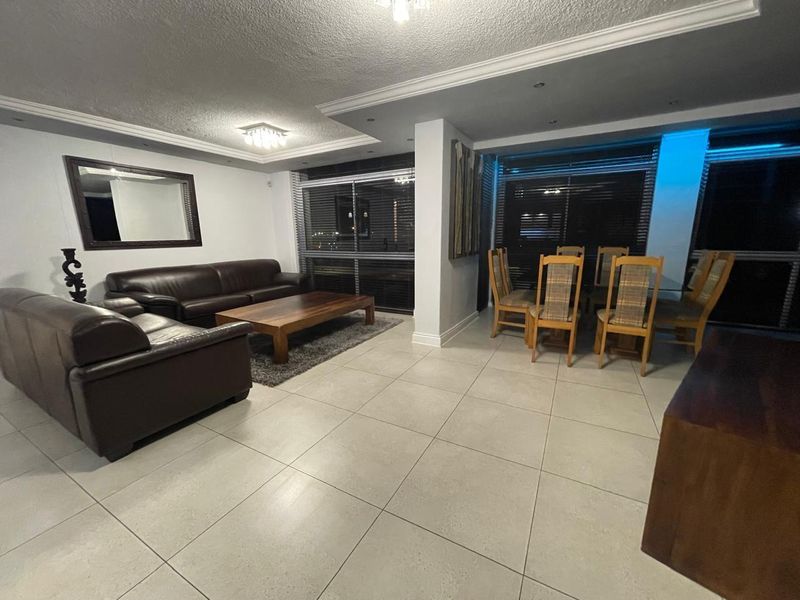 Spacious open-plan living and dining area featuring large windows with venetian blinds, neutral tiled flooring, and modern recessed ceiling lighting.