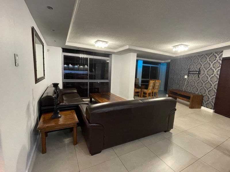 Spacious open-plan living and dining area featuring tiled floors, decorative wallpaper, recessed lighting, and large windows with venetian blinds.