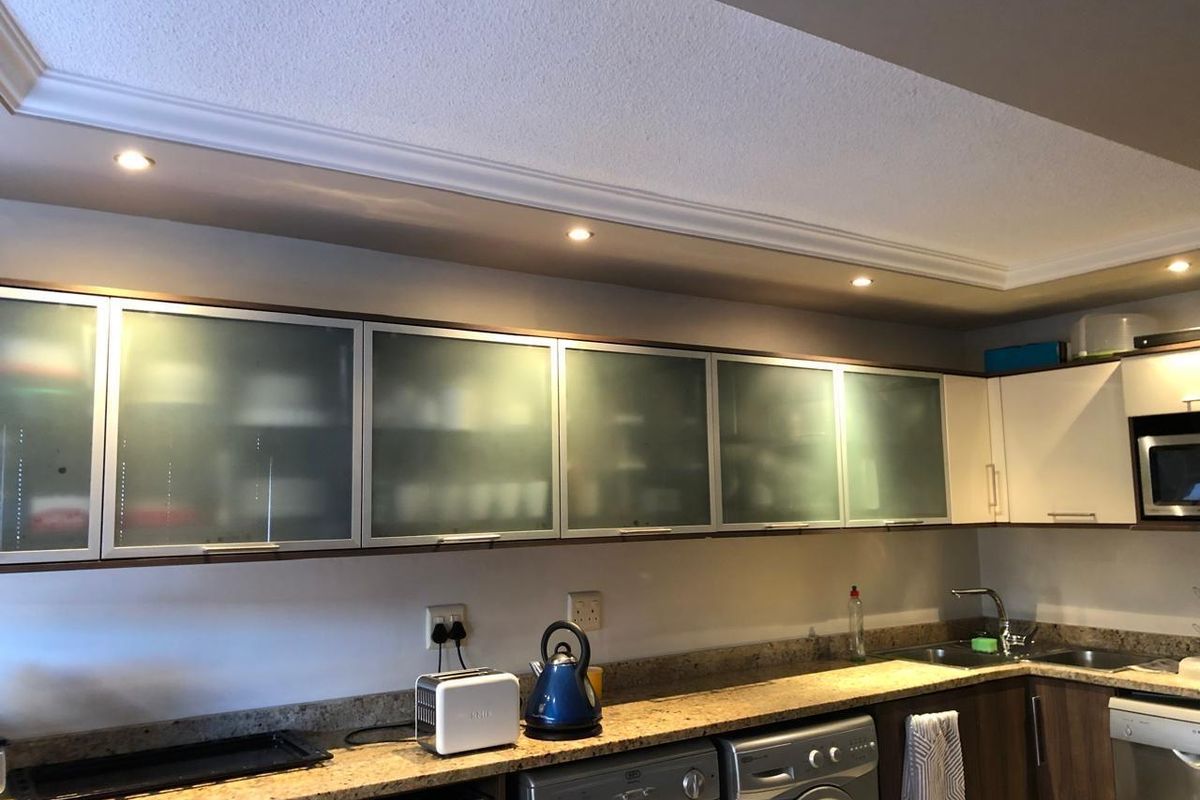 A functional kitchen featuring frosted glass upper cabinetry, granite countertops, stainless steel sink, and integrated lighting with a modern, clean aesthetic.