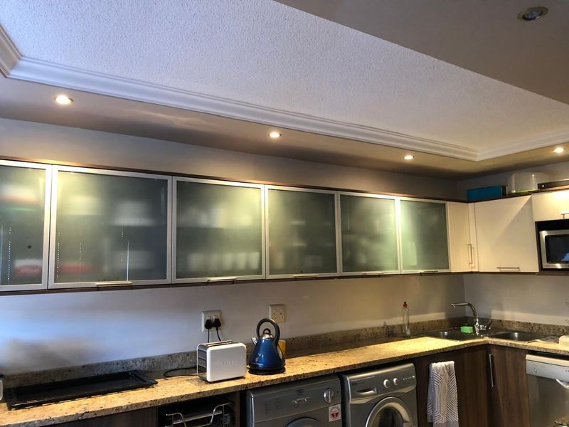 A functional kitchen featuring frosted glass upper cabinetry, granite countertops, stainless steel sink, and integrated lighting with a modern, clean aesthetic.