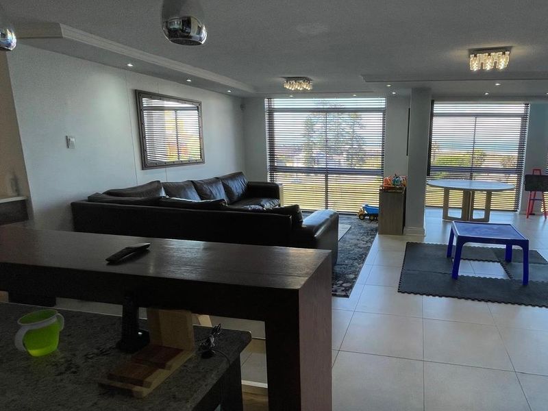 Spacious open-plan living area featuring tiled floors, recessed lighting, and large windows with venetian blinds, seamlessly connecting to a kitchen breakfast bar.