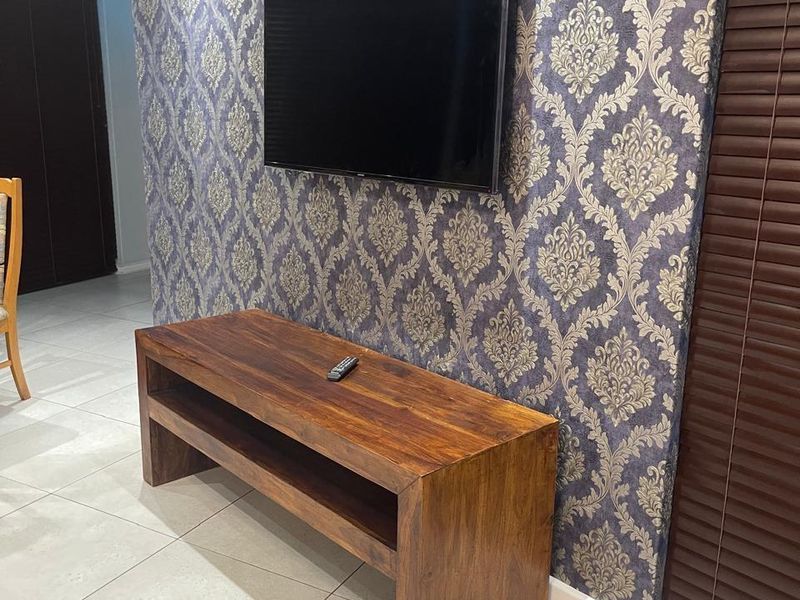 A living room area featuring decorative patterned wallpaper, neutral ceramic floor tiles, recessed ceiling lighting, and dark wood venetian blinds.