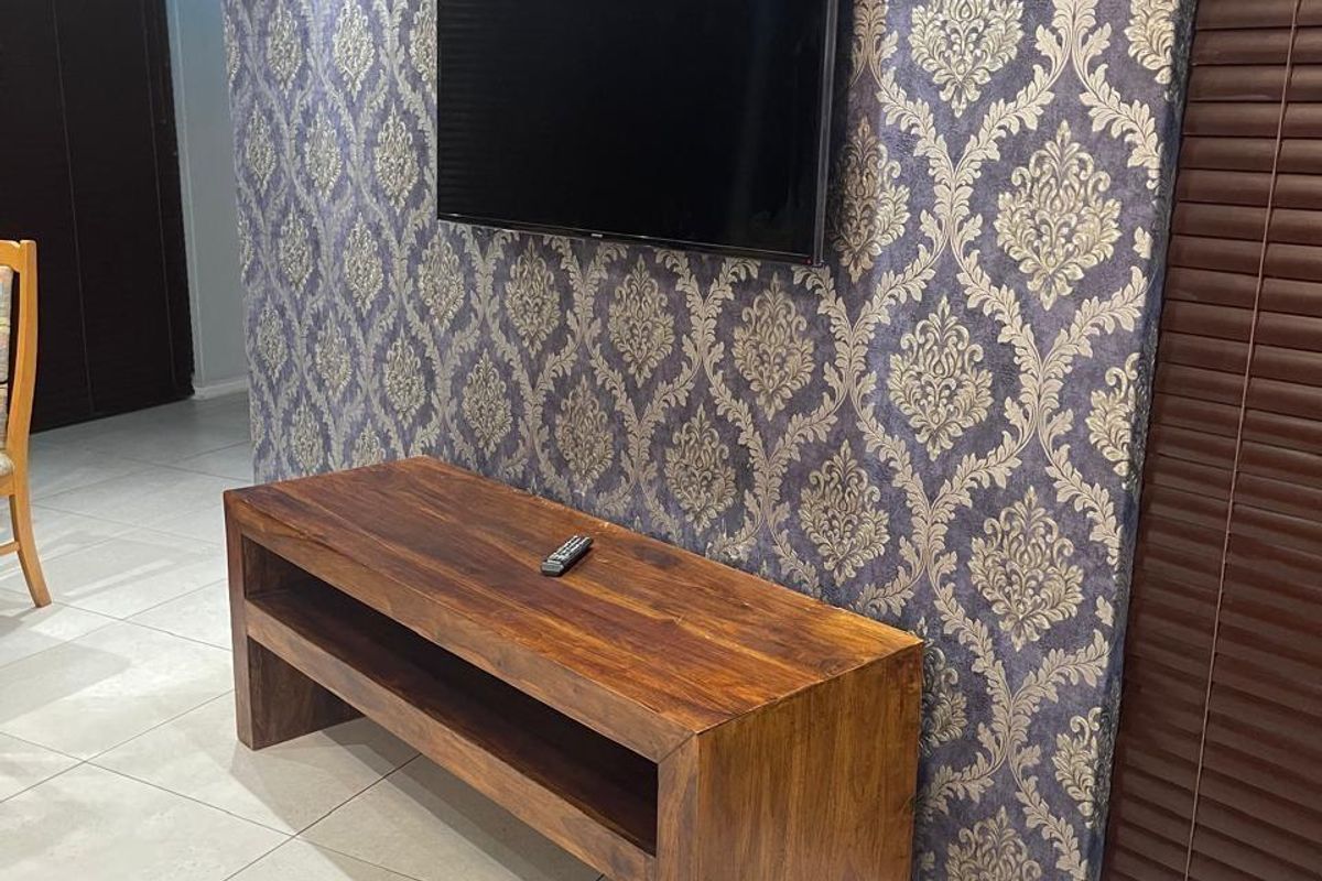 A living room area featuring decorative patterned wallpaper, neutral ceramic floor tiles, recessed ceiling lighting, and dark wood venetian blinds.