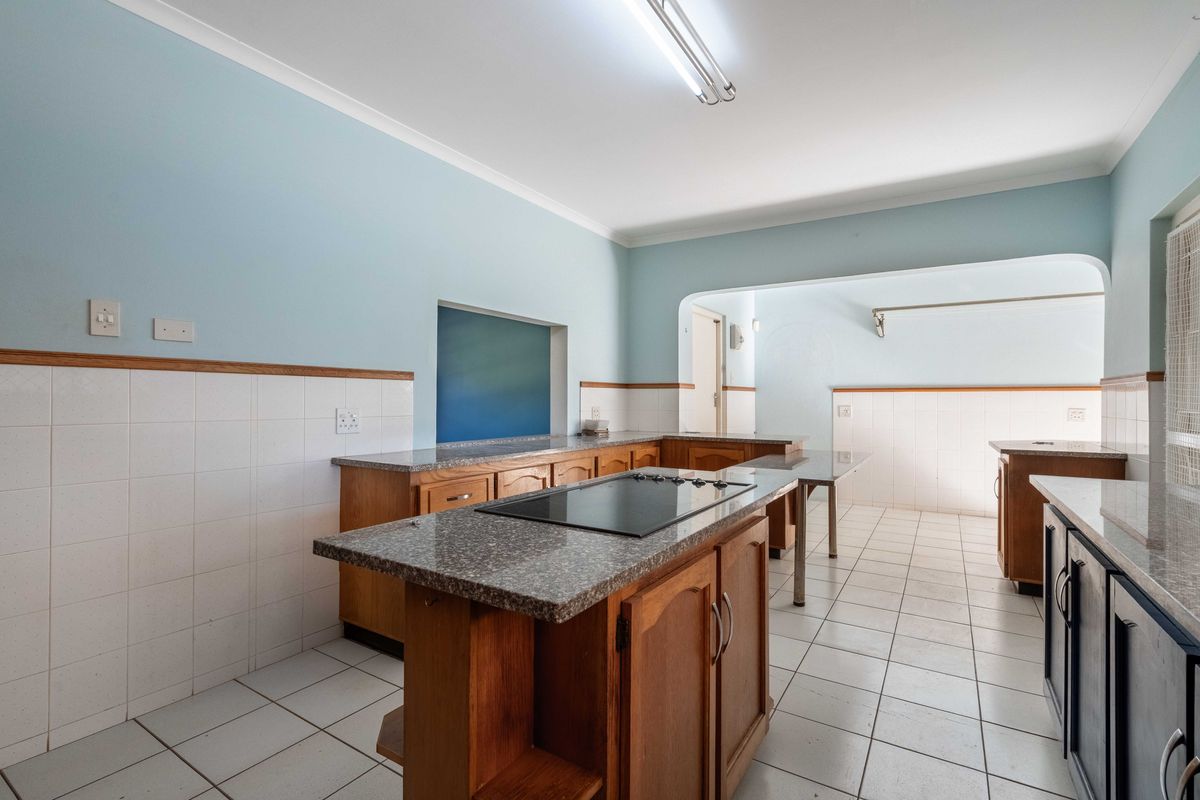 Spacious kitchen featuring wooden cabinetry, granite countertops, integrated electric hob, and tiled flooring, offering a functional layout ready for modern updates.