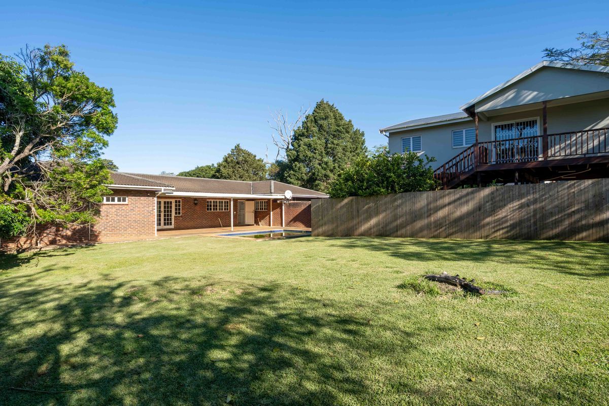 Spacious rear garden featuring a swimming pool, covered patio area, and established lawn, set against a brick residential structure.
