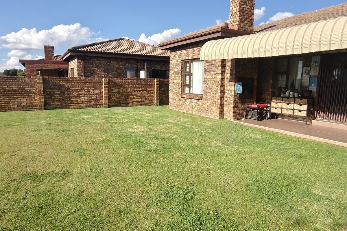 A spacious rear garden featuring a well-maintained lawn, a covered patio with a built-in braai, and classic face brick exterior finishes.