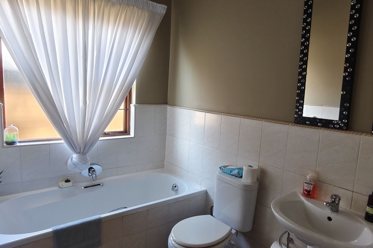 A functional bathroom featuring a bathtub, pedestal basin, and toilet with neutral wall tiling and natural light from the window.