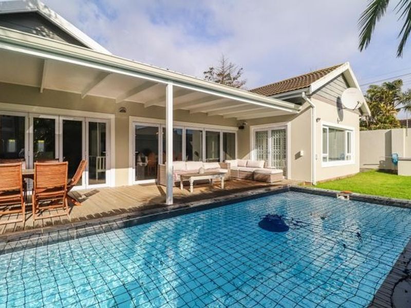 A well-maintained outdoor area featuring a swimming pool with a safety net, adjacent to a covered timber deck and patio with glass door access.